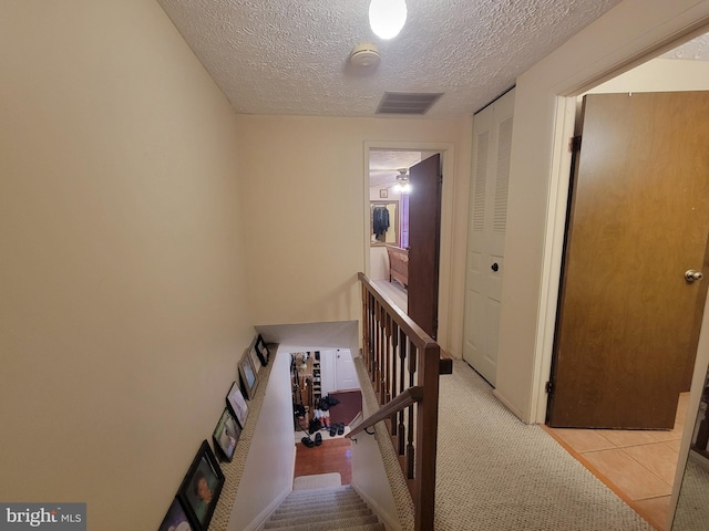 corridor featuring visible vents, a textured ceiling, and an upstairs landing