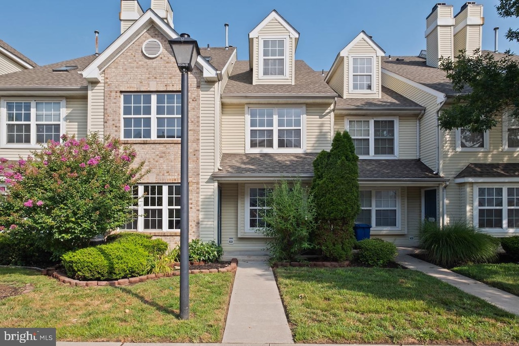 townhome / multi-family property featuring roof with shingles, brick siding, and a front lawn