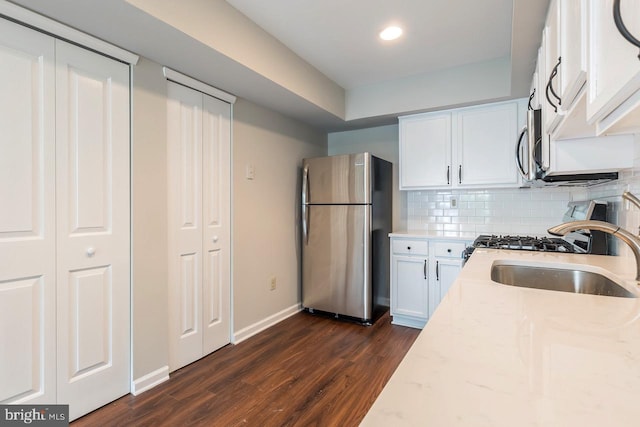 kitchen with decorative backsplash, appliances with stainless steel finishes, white cabinetry, a sink, and light stone countertops