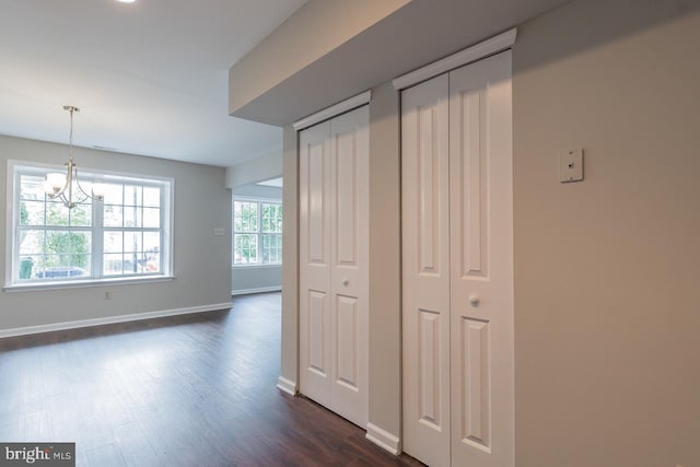 hall featuring dark wood-style floors, a chandelier, and baseboards