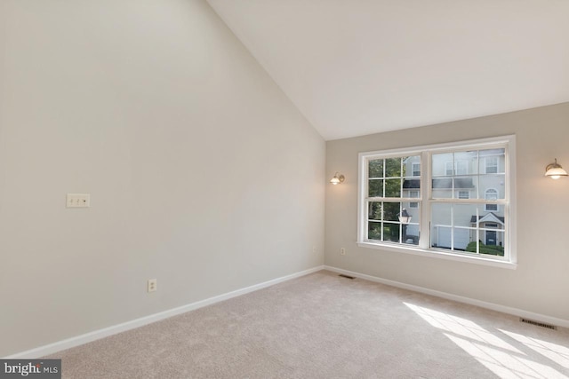 spare room with baseboards, vaulted ceiling, visible vents, and light colored carpet