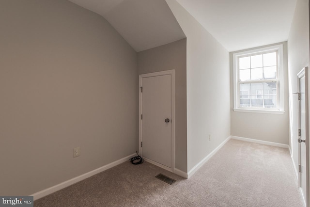 interior space with vaulted ceiling, light colored carpet, visible vents, and baseboards