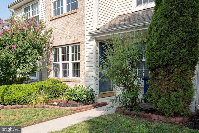 view of exterior entry featuring brick siding and a shingled roof