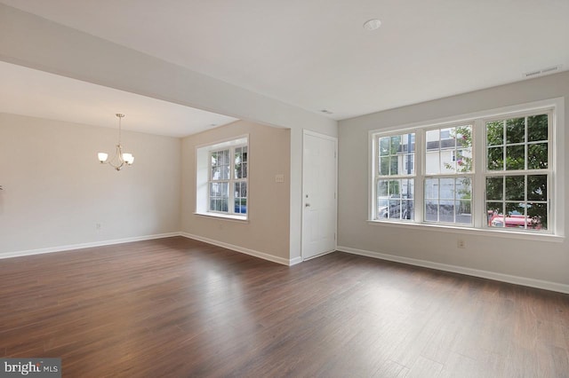 spare room featuring dark wood-style flooring, a notable chandelier, and baseboards