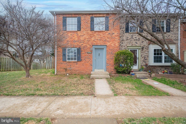 view of front of house with brick siding, a front yard, and fence