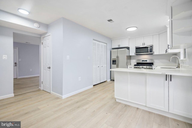 kitchen featuring light wood finished floors, a peninsula, stainless steel appliances, light countertops, and a sink