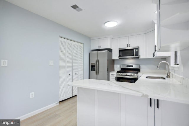 kitchen featuring light stone counters, a peninsula, a sink, visible vents, and appliances with stainless steel finishes