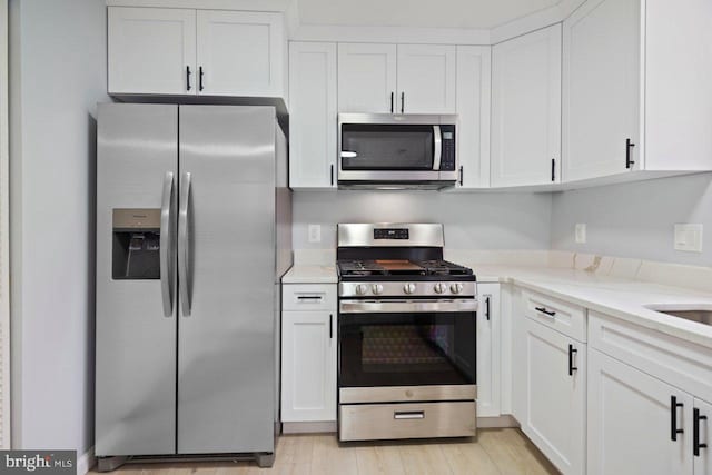 kitchen with white cabinets, light wood-style floors, light stone counters, and stainless steel appliances