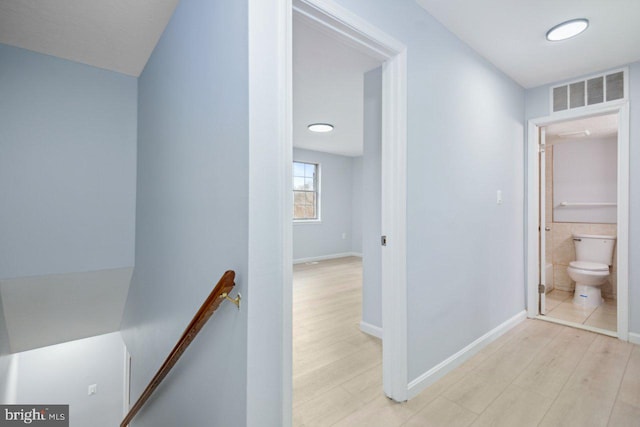 hall featuring baseboards, visible vents, light wood finished floors, and an upstairs landing