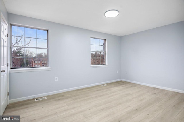 empty room with light wood-style flooring, visible vents, and baseboards