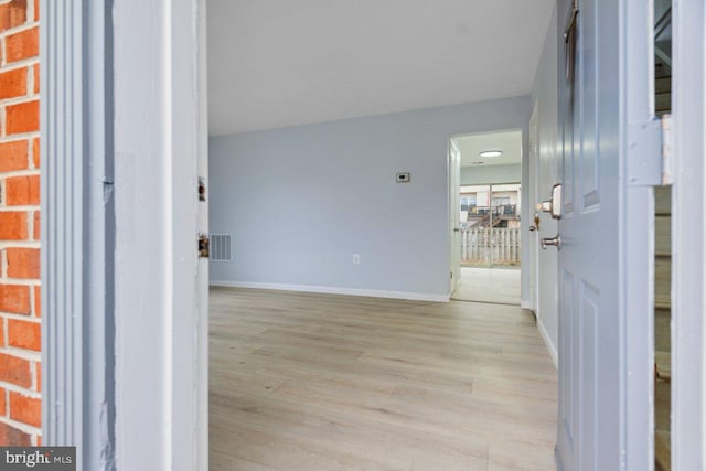 corridor with baseboards, visible vents, and light wood finished floors