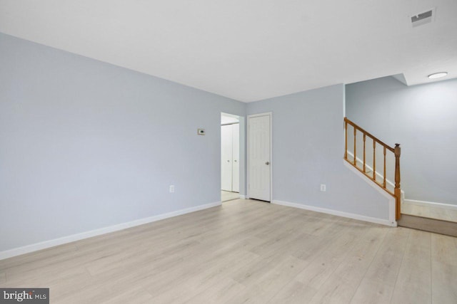 unfurnished room featuring stairs, light wood-style flooring, visible vents, and baseboards