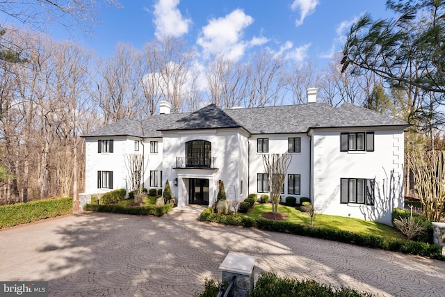 view of front of property featuring a balcony, a high end roof, stucco siding, and a chimney