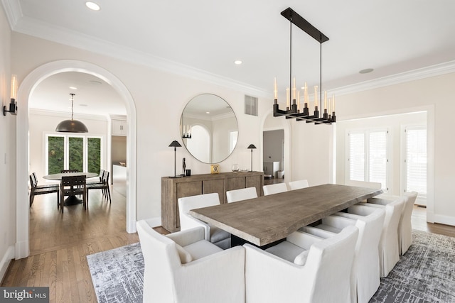 dining space with arched walkways, recessed lighting, crown molding, and wood finished floors