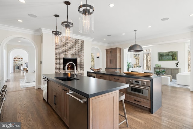 kitchen with dark countertops, a kitchen island with sink, oven, and a sink