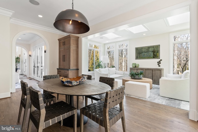 dining room with a wealth of natural light, light wood-type flooring, arched walkways, and ornamental molding