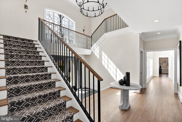 stairs with a notable chandelier, wood finished floors, a high ceiling, crown molding, and baseboards