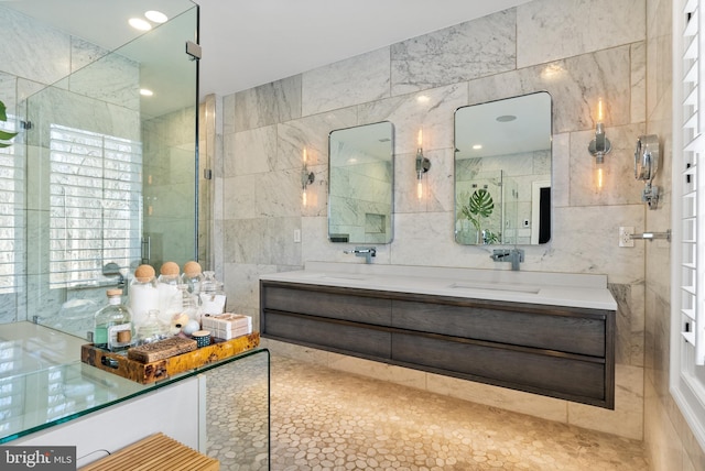 bathroom with double vanity, a shower with door, tile walls, and a sink