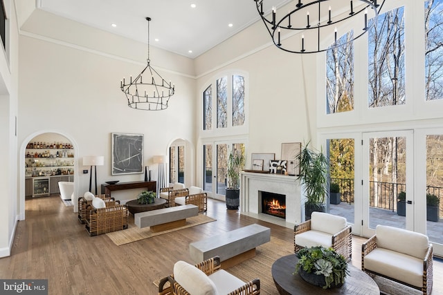 interior space featuring a lit fireplace, french doors, wood finished floors, arched walkways, and a notable chandelier