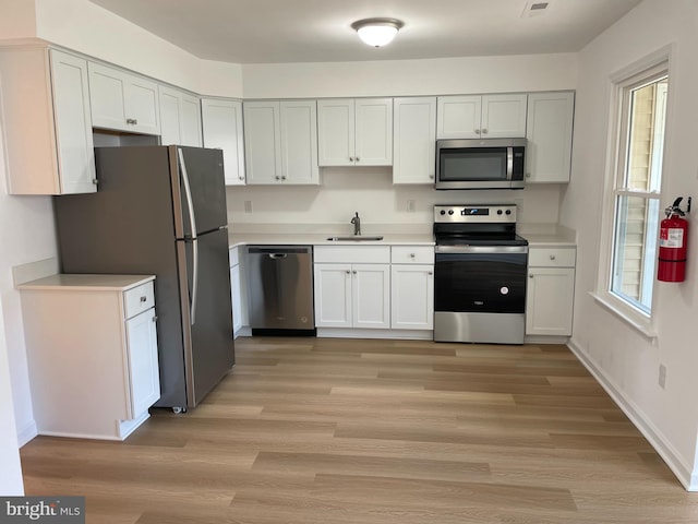 kitchen with stainless steel appliances, light countertops, a sink, and white cabinetry