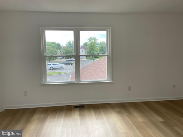 spare room with light wood-type flooring, visible vents, and baseboards