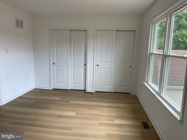 unfurnished bedroom featuring light wood finished floors, two closets, visible vents, and baseboards