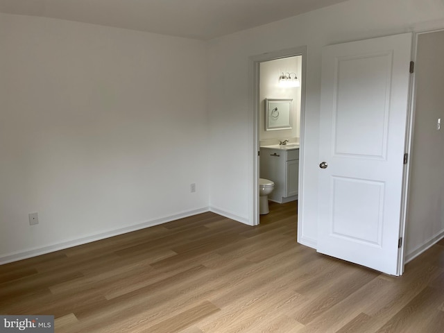 unfurnished bedroom featuring light wood-style flooring, baseboards, a sink, and ensuite bathroom