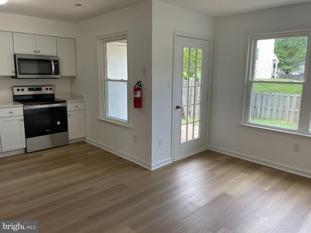 kitchen with light wood-style flooring, white cabinets, light countertops, appliances with stainless steel finishes, and a wealth of natural light