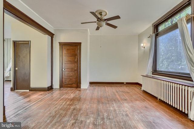 spare room featuring light wood-style flooring, radiator heating unit, ornamental molding, ceiling fan, and baseboards