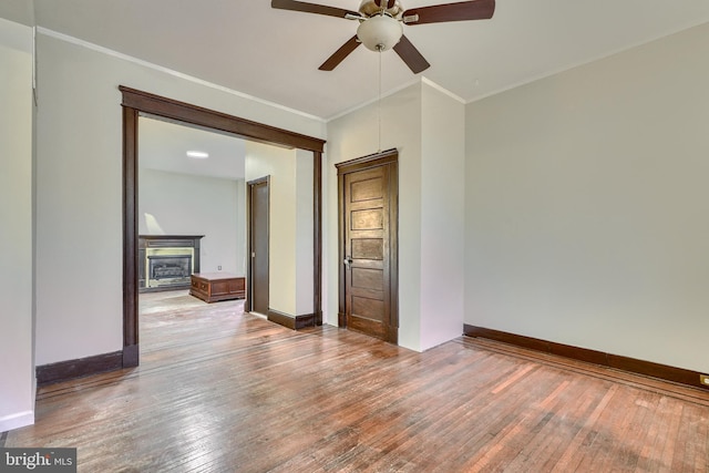 spare room with baseboards, ceiling fan, ornamental molding, wood finished floors, and a fireplace