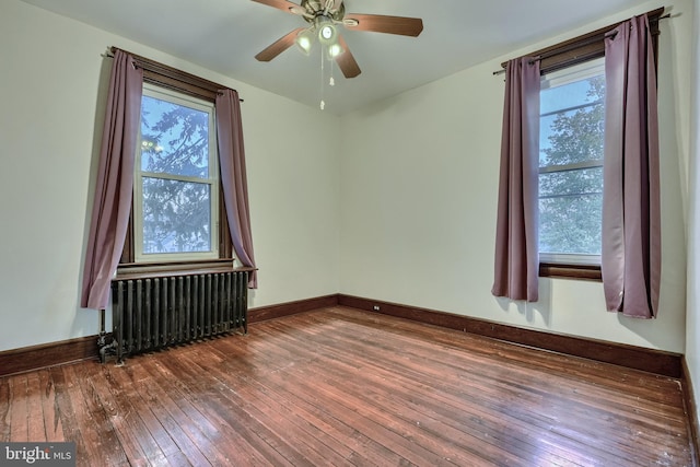 spare room with baseboards, dark wood finished floors, radiator heating unit, and ceiling fan