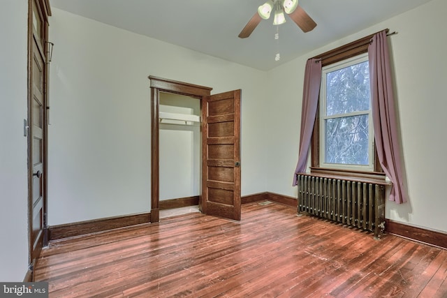 unfurnished bedroom with dark wood-style floors, radiator heating unit, baseboards, and ceiling fan