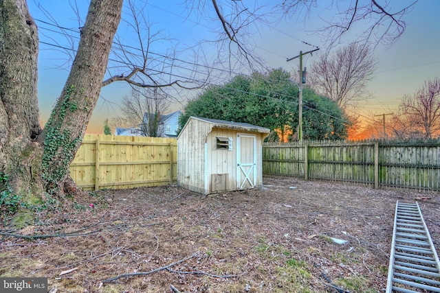 yard at dusk featuring a fenced backyard, an outdoor structure, and a shed