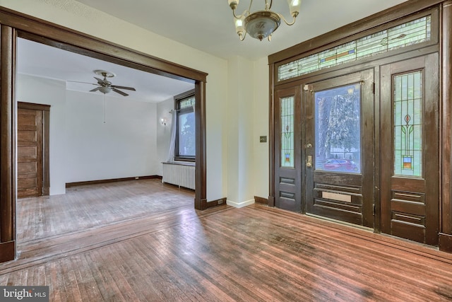 foyer with ceiling fan with notable chandelier, baseboards, radiator heating unit, and wood finished floors