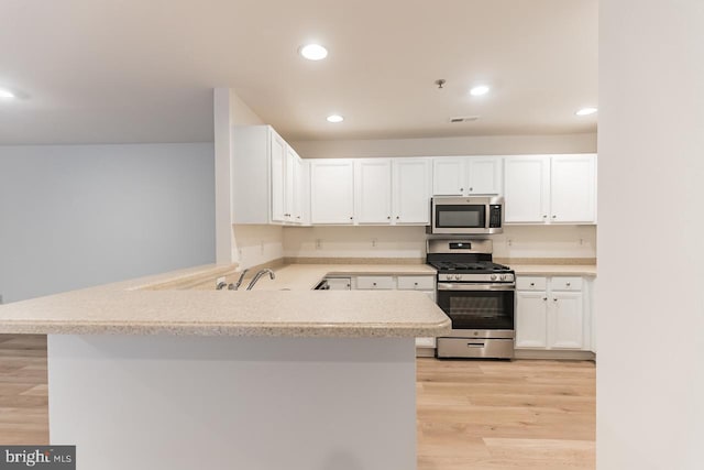 kitchen with light wood-style flooring, stainless steel appliances, a peninsula, white cabinetry, and light countertops