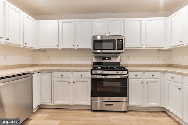 kitchen with appliances with stainless steel finishes, light countertops, light wood-style flooring, and white cabinetry