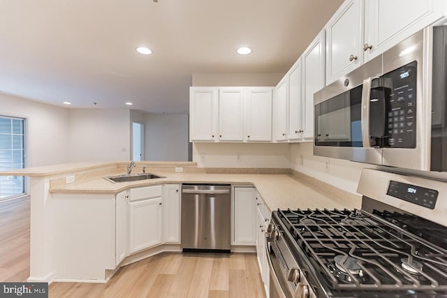 kitchen with stainless steel appliances, light countertops, white cabinets, a sink, and a peninsula