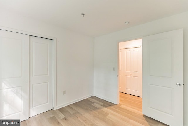 unfurnished bedroom featuring light wood finished floors, a closet, and baseboards