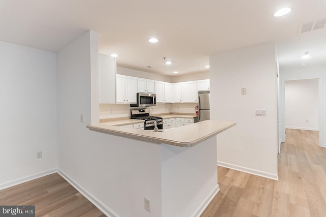 kitchen featuring light countertops, appliances with stainless steel finishes, white cabinetry, light wood-type flooring, and a peninsula