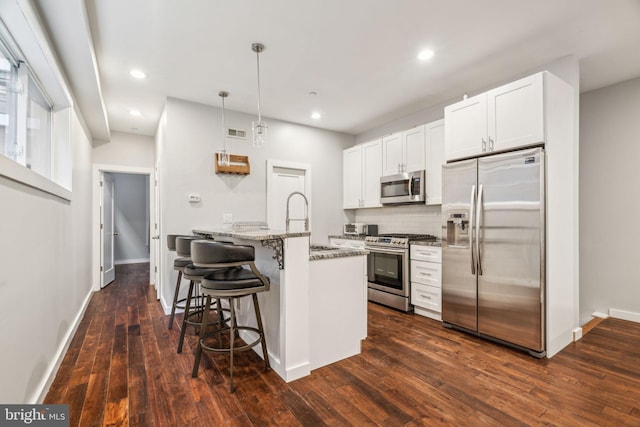 kitchen featuring appliances with stainless steel finishes, a breakfast bar, dark wood finished floors, and light stone countertops