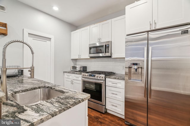 kitchen with decorative backsplash, dark wood finished floors, appliances with stainless steel finishes, dark stone countertops, and a sink