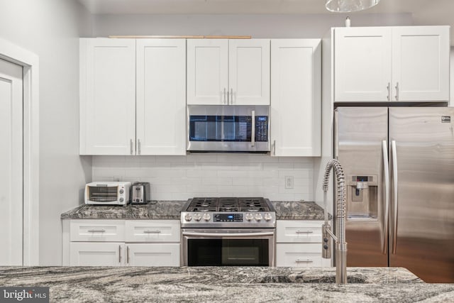 kitchen featuring dark stone counters, stainless steel appliances, and white cabinetry