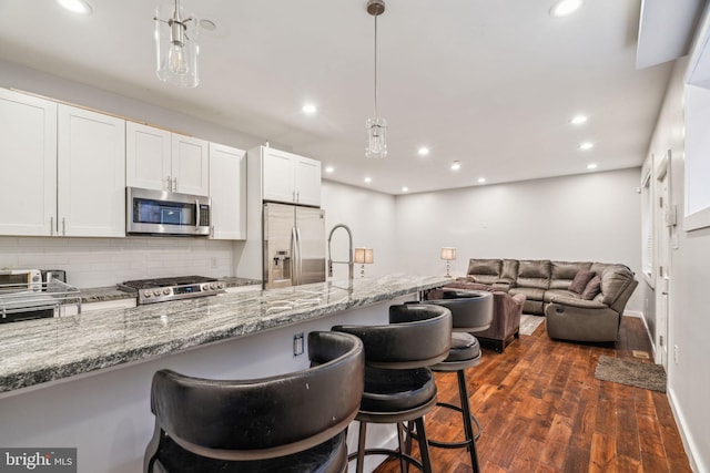 kitchen featuring light stone counters, a breakfast bar, dark wood-style floors, decorative backsplash, and appliances with stainless steel finishes