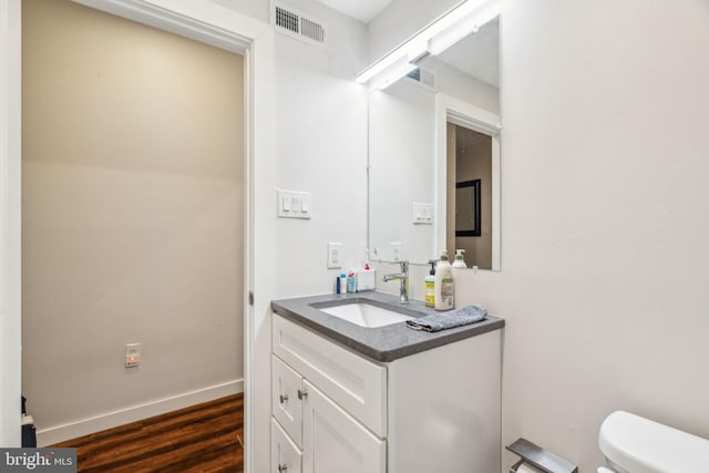 half bathroom with visible vents, toilet, vanity, wood finished floors, and baseboards