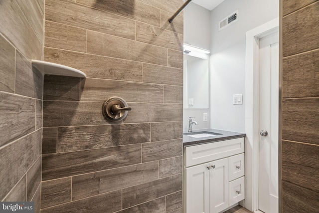 bathroom featuring visible vents, tiled shower, and vanity