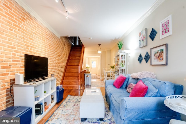 living room featuring brick wall, stairway, wood finished floors, crown molding, and track lighting