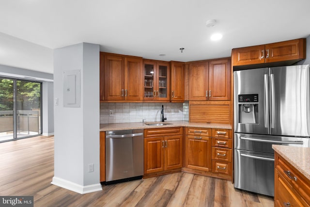 kitchen featuring light stone counters, a sink, appliances with stainless steel finishes, backsplash, and brown cabinetry