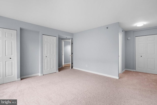 unfurnished bedroom featuring light carpet, two closets, and baseboards