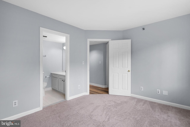 unfurnished bedroom featuring light colored carpet, ensuite bath, and baseboards