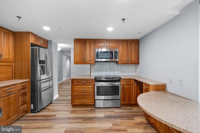 kitchen featuring appliances with stainless steel finishes, brown cabinetry, decorative backsplash, and wood finished floors